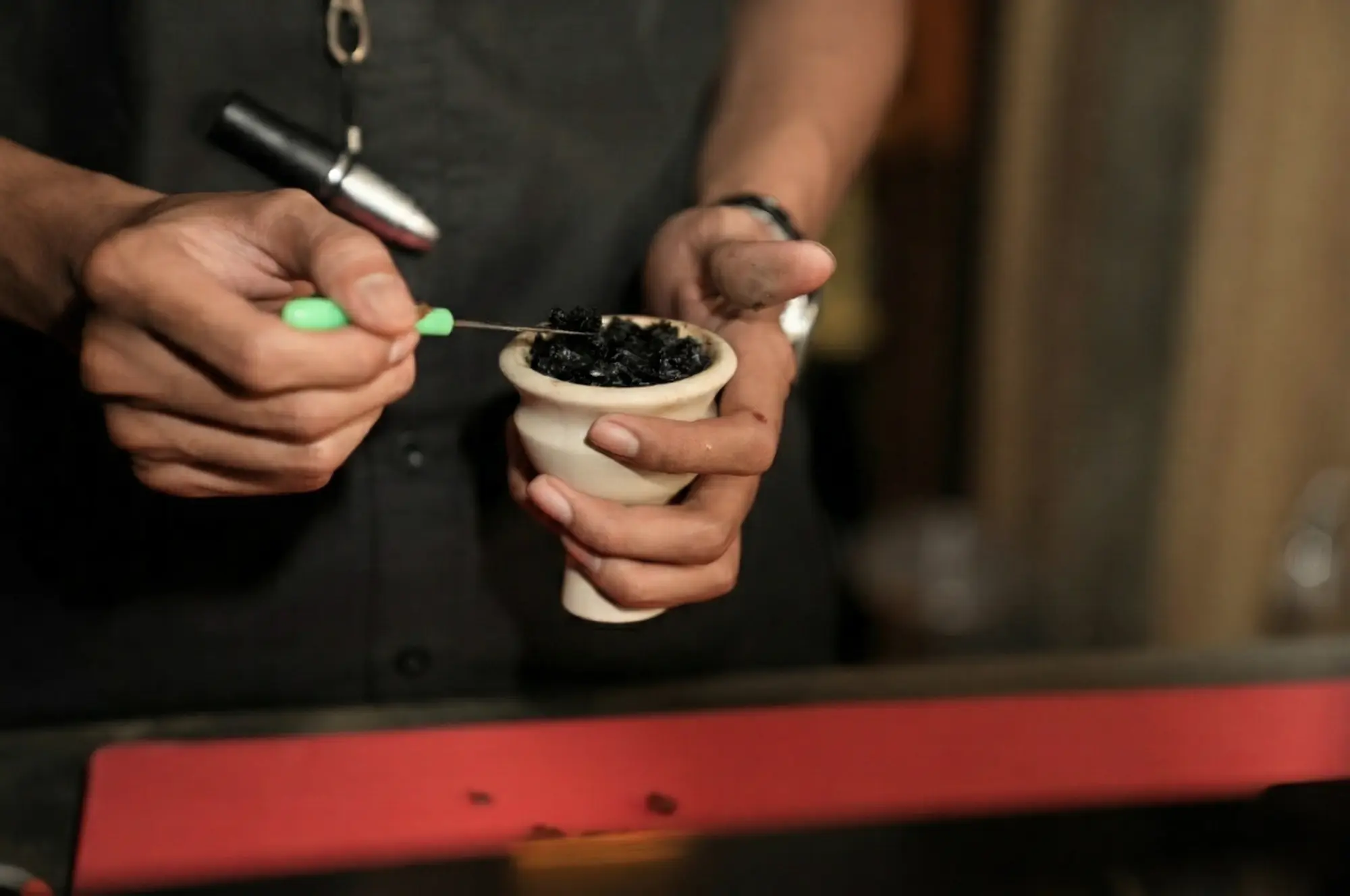 A close-up shot of a person's hands professionally packing a custom hookah flavor mix into a clay shisha bowl using a packing tool.