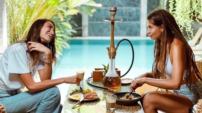 Two happy women enjoying brunch and a hookah session by the pool at Eden Hookah Club Seminyak, the perfect daytime answer to where to smoke & buy Mezza in Bali.